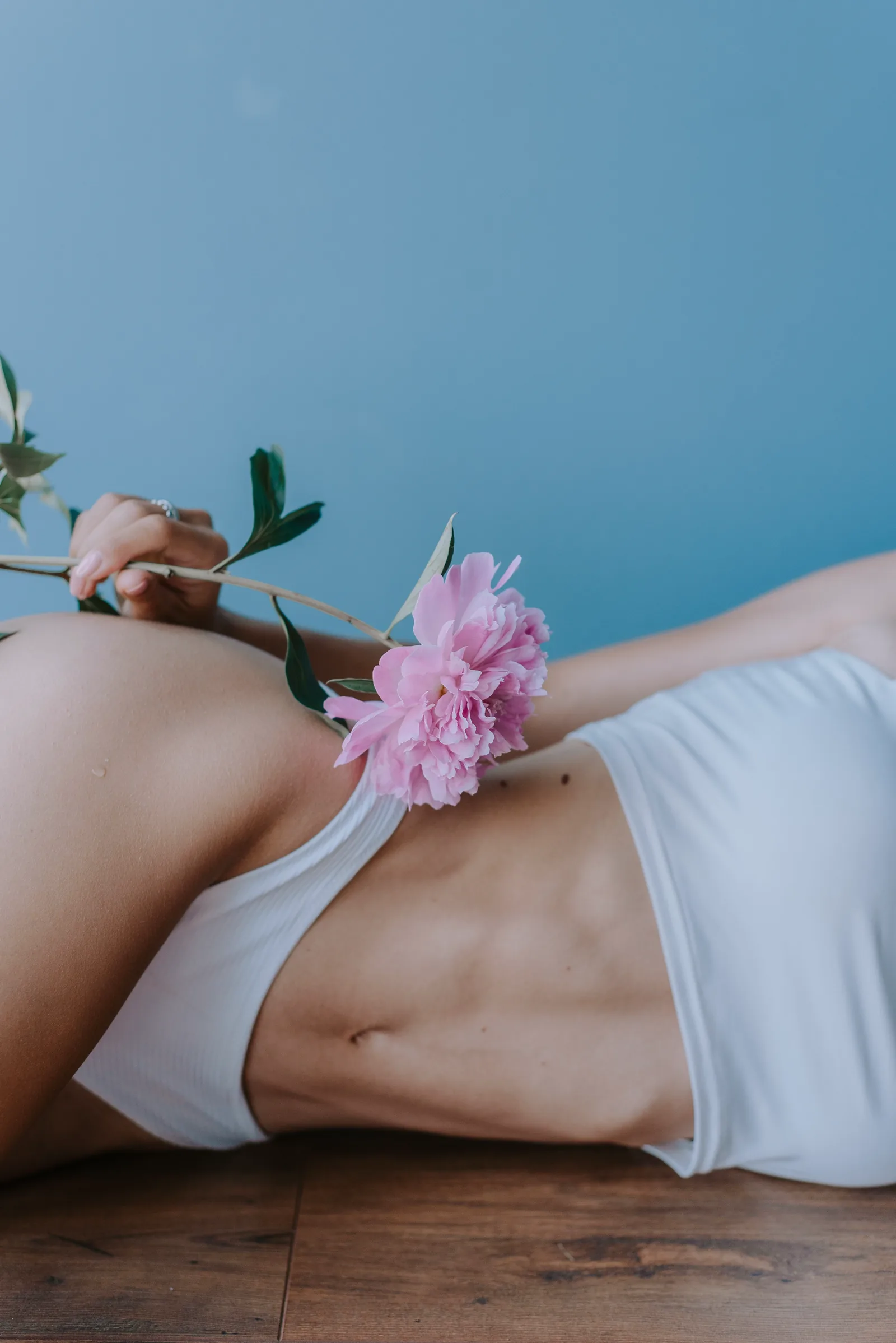 Woman resting with a peony flower across her abdomen